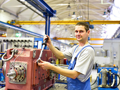 Ein Arbeiter in einer Fabrik, der ein Werkzeug an einer Maschinenkomponente verwendet.
